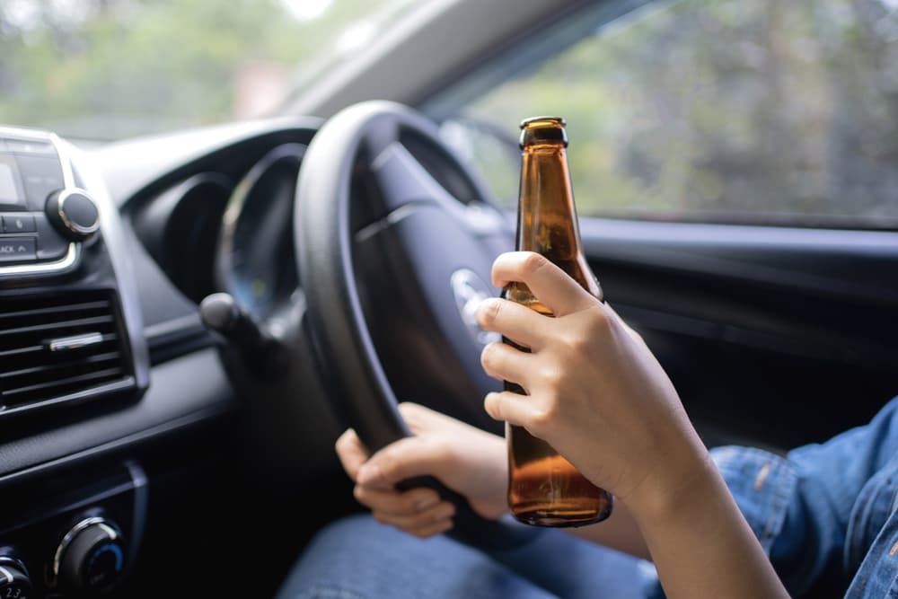 Image depicting a woman drinking from a beer bottle while operating a car, illustrating the dangerous concept of driving while intoxicated.