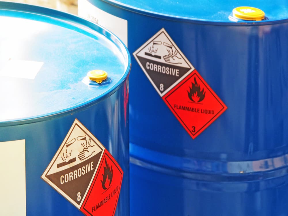 Close-up of blue hazardous chemical barrels with corrosive and flammable warning labels in daylight.