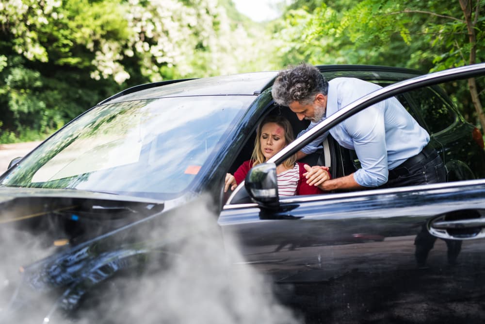 A man assisting a young woman out of a car following a car accident.