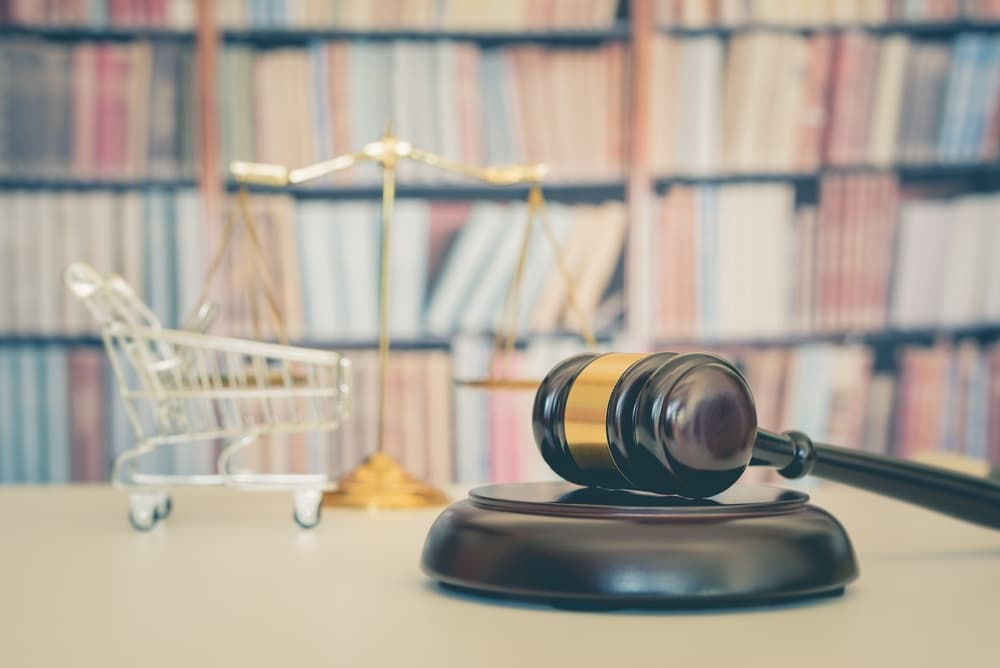 Wooden judge gavel, shopping cart, balanced scale of justice on a table, symbolizing consumer rights and protection in business law.