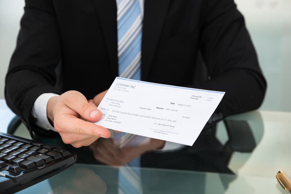 Insurance agent showing cheque at desk in office