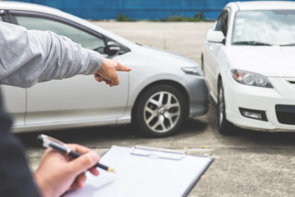 An insurance agent inspects a damaged car and fills out a claim report form after an accident. Traffic accident and insurance concept.