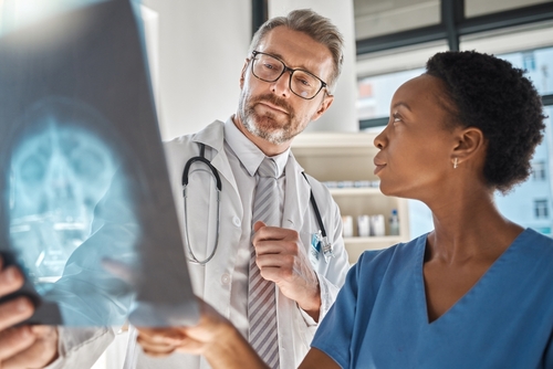 A doctor and a nurse are examining an X-ray image together in a medical setting, discussing the findings, with the focus on the X-ray held by the doctor.