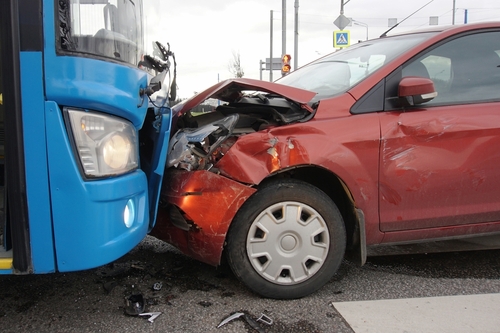 A blue bus and a red car involved in a head-on collision, with significant damage to the front end of both vehicles.