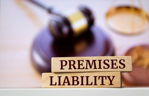 A legal-themed image featuring wooden blocks with the words "Premises Liability" in front of a blurred background with a gavel and scales of justice.