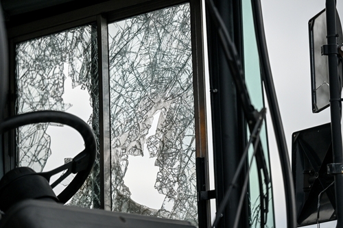 A close-up of a shattered bus windshield with cracks radiating across the glass, showing the aftermath of an accident.