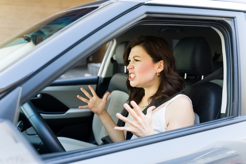 A frustrated woman sitting in the driver's seat of a car, angrily gesturing with her hands, showing signs of road rage.