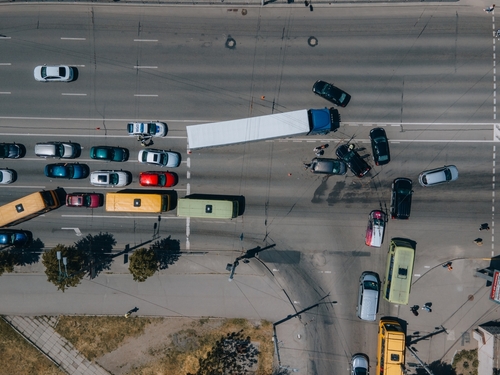 An aerial view of a multi-vehicle accident at an intersection involving a large truck and several cars, with traffic congestion and emergency responders present.