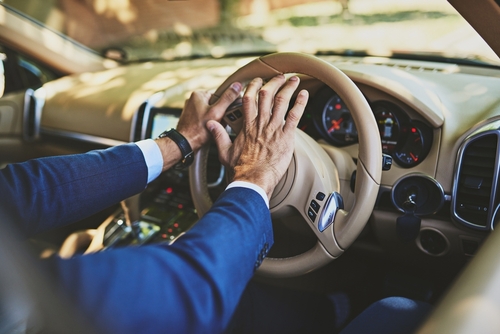 A close-up of a driver's hands forcefully pressing the car horn, reflecting frustration or anger, commonly associated with road rage.