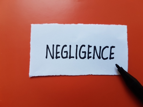 A piece of white paper with the word "NEGLIGENCE" written in bold black letters on an orange background, with a black pen pointing towards the word.