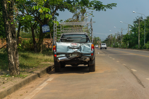 A pickup truck with significant rear-end damage is parked on the side of a road in a rural area.