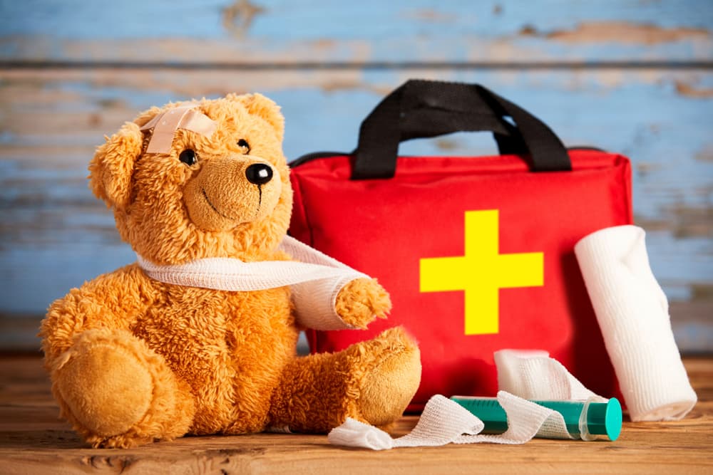 Child injury concept with a little teddy bear with its arm in a sling alongside a first aid kit and bandages on rustic wood