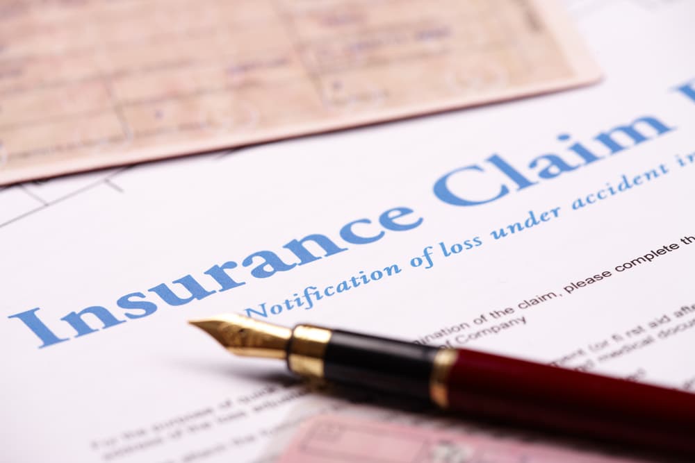 Blank insurance claim form and other papers like ID or vehicle documents and pen lying on desk