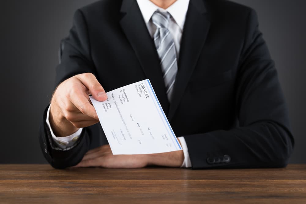 Close-up Of Businessperson Giving Cheque At Wooden Desk