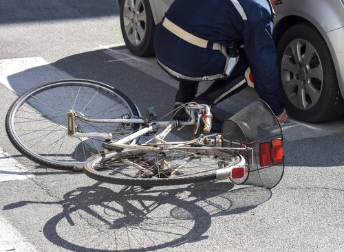 A cyclist on the ground near a car after an apparent accident, with a bicycle laying overturned in the street.