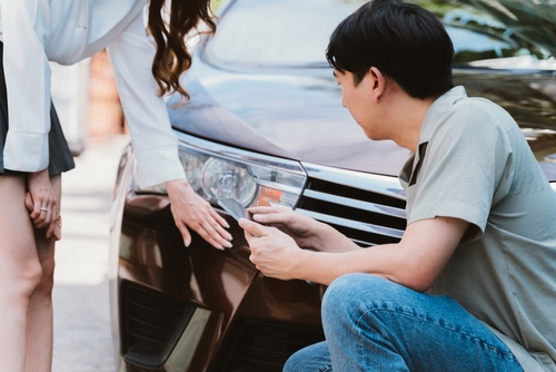 Two individuals inspecting a minor car accident, focusing on the damage to the front of the vehicle's headlight and bumper.