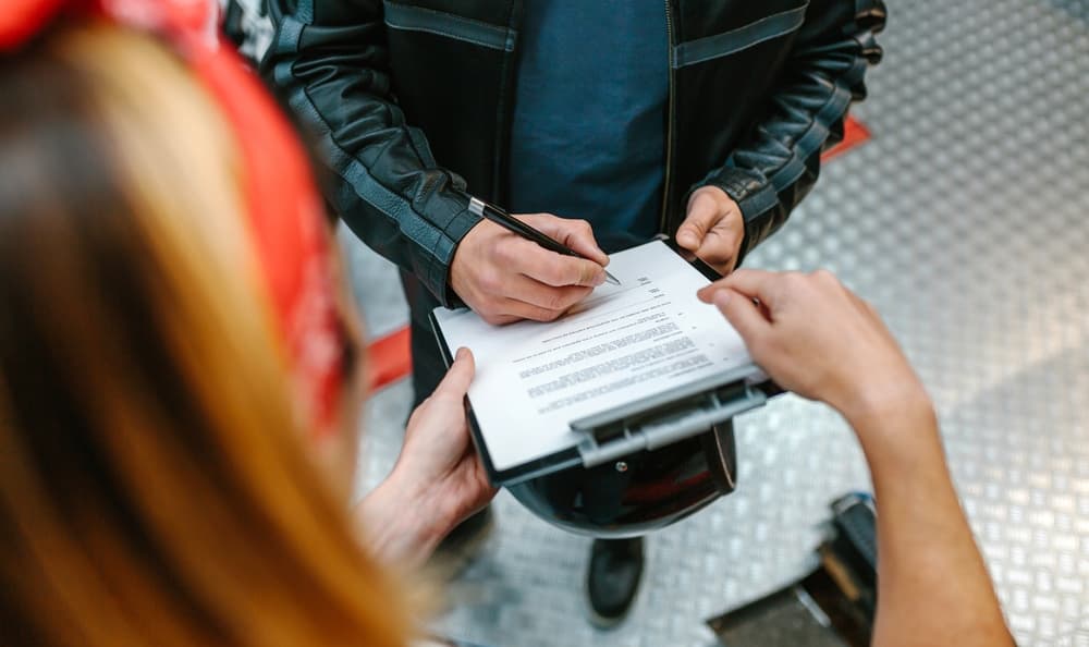 Biker man wearing leather jacket signing insurance policy to receipt his repaired motorcycle.