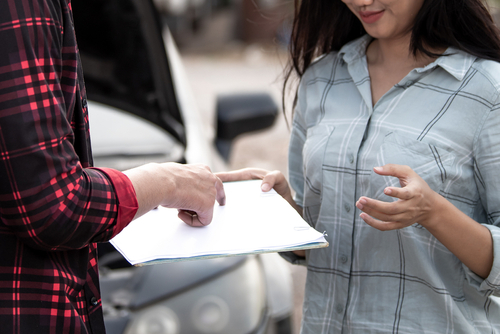 Two people standing beside a damaged car reviewing paperwork after a car accident.