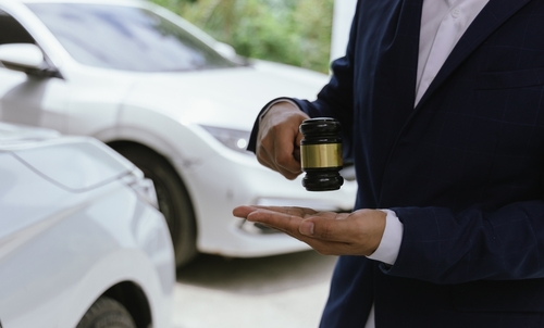 Lawyer holding a gavel near parked cars while discussing a car accident claim.
