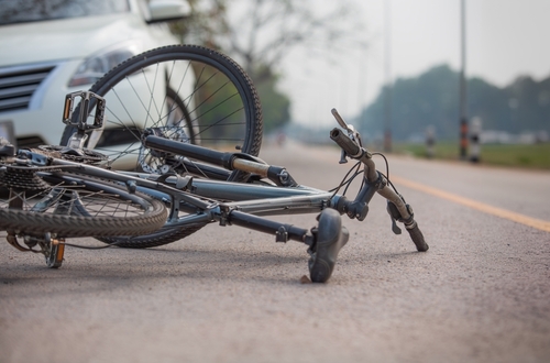 Damaged bicycle lying on the road in front of a white car after a traffic collision.