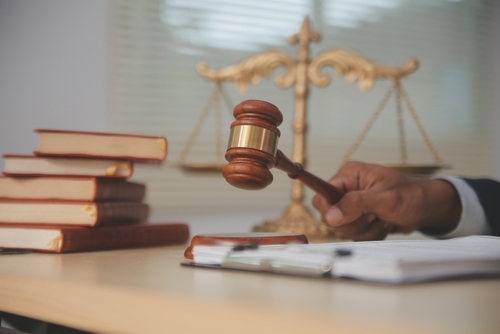 Judge holding a gavel in a courtroom with law books stacked beside a golden scale of justice.