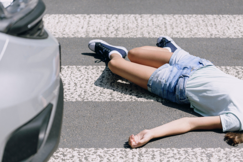 A young person lies injured on a crosswalk after being hit by a car, showing the aftermath of a pedestrian accident.