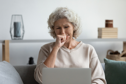 Elderly woman sitting on a couch looking emotional while using a laptop.