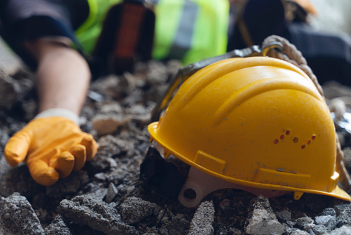 Construction helmet lying on debris near an injured worker’s hand, illustrating severe construction site accidents and head injuries.