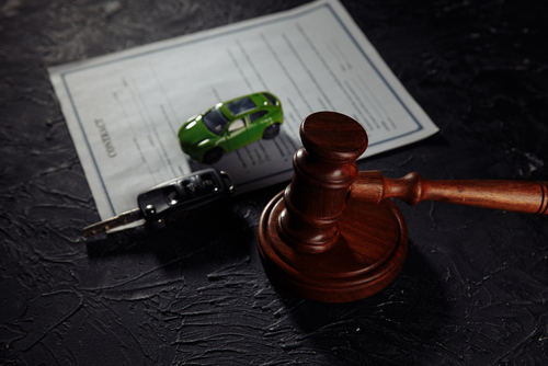A judge’s gavel, car keys, and a small green toy car placed on a legal document symbolizing a car accident claim.
