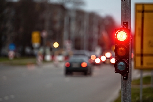 Red traffic light at a busy city intersection with blurred cars in the background at dusk.