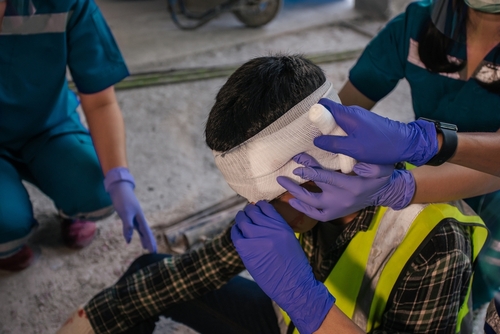 Injured construction worker receiving first aid for a head wound at a job site, representing Gainesville brain injury claims.