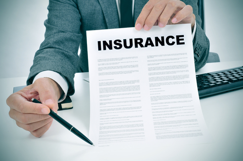 A man in a business suit holding an insurance document and pointing with a pen, symbolizing an insurance claim or policy discussion.