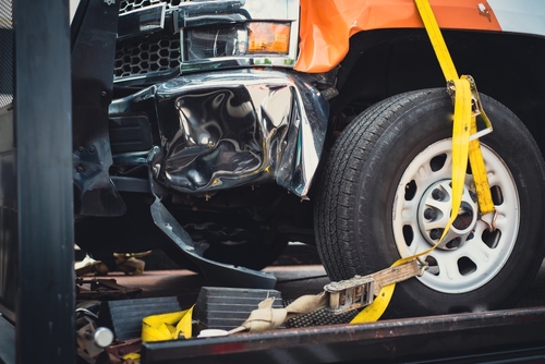 Tow truck securing a damaged vehicle with yellow straps after an accident.