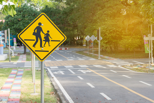 A yellow school zone pedestrian crossing sign beside a road, reminding drivers to slow down and watch for children.