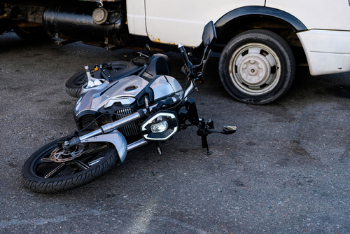 A damaged motorcycle lying on the ground after a collision with a white van.