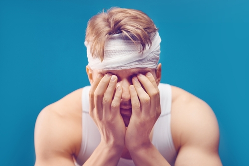 Injured man with a head bandage covering his face with his hands, representing cases handled by an Ocala brain injury lawyer.