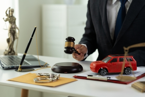 A Gainesville car accident lawyer represented through a courtroom desk with a gavel, scale, documents, and a red toy SUV symbolizing legal help after a crash.