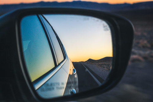 Rearview mirror photo of a car driving at sunset on an open road, used to illustrate how a Gainesville car accident lawyer helps clients after serious collisions.