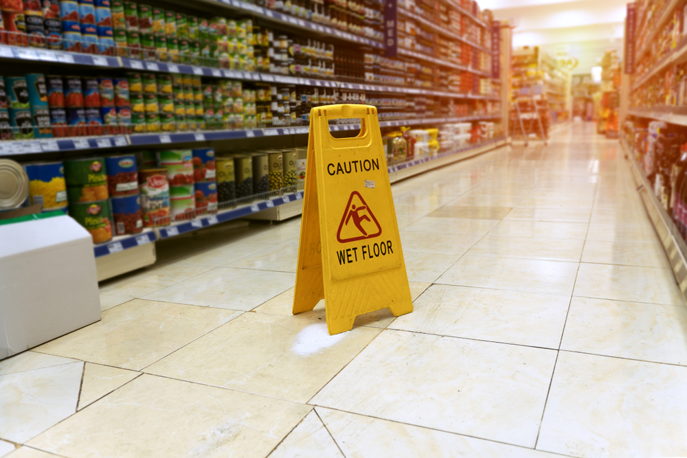 Caution wet floor sign in grocery store aisle with spill on tile floor, illustrating premises hazard for a Gainesville slip and fall accident lawyer case.