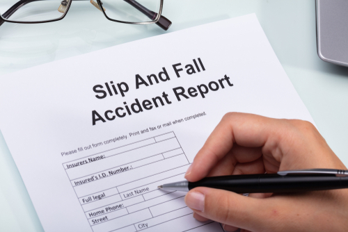 Hand filling out slip and fall accident report form at hotel, case reviewed by a Daytona slip and fall accident lawyer.