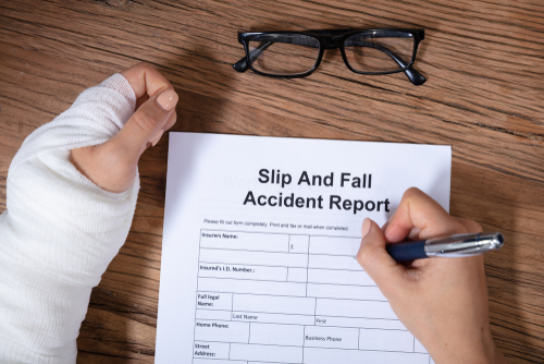 Person with bandaged hand completing a slip and fall accident report form, highlighting case preparation by a Gainesville Slip and Fall Accident Lawyer.