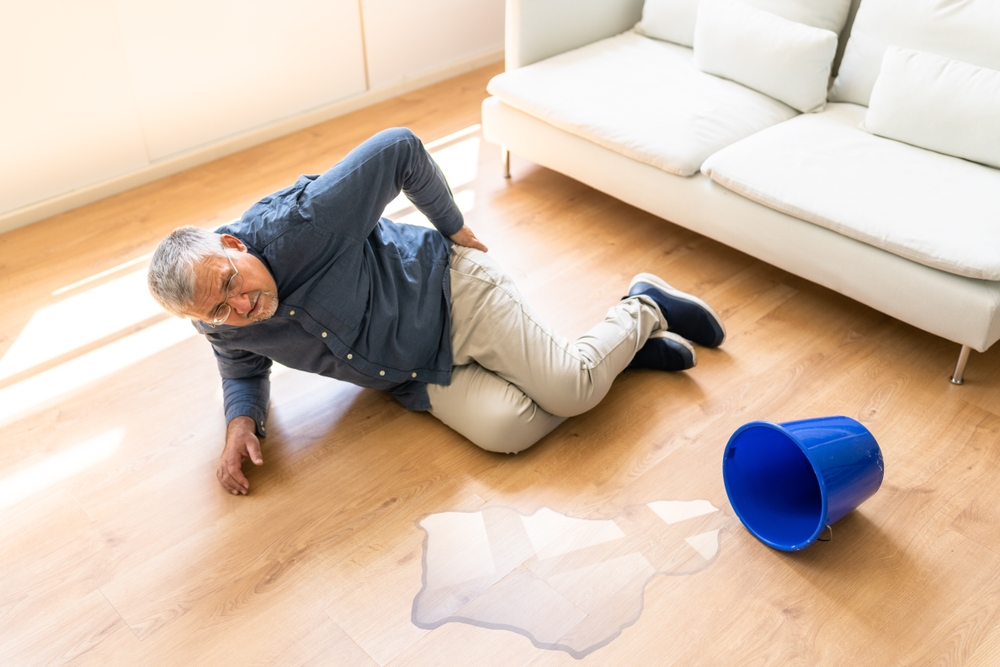 Elderly man on floor beside spilled water and bucket in home, example of case handled by a Gainesville Slip and Fall Accident Lawyer.