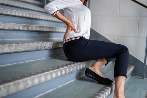 Woman sitting on metal stairs holding lower back in pain after a fall, illustrating injuries handled by a Gainesville Slip and Fall Accident Lawyer.