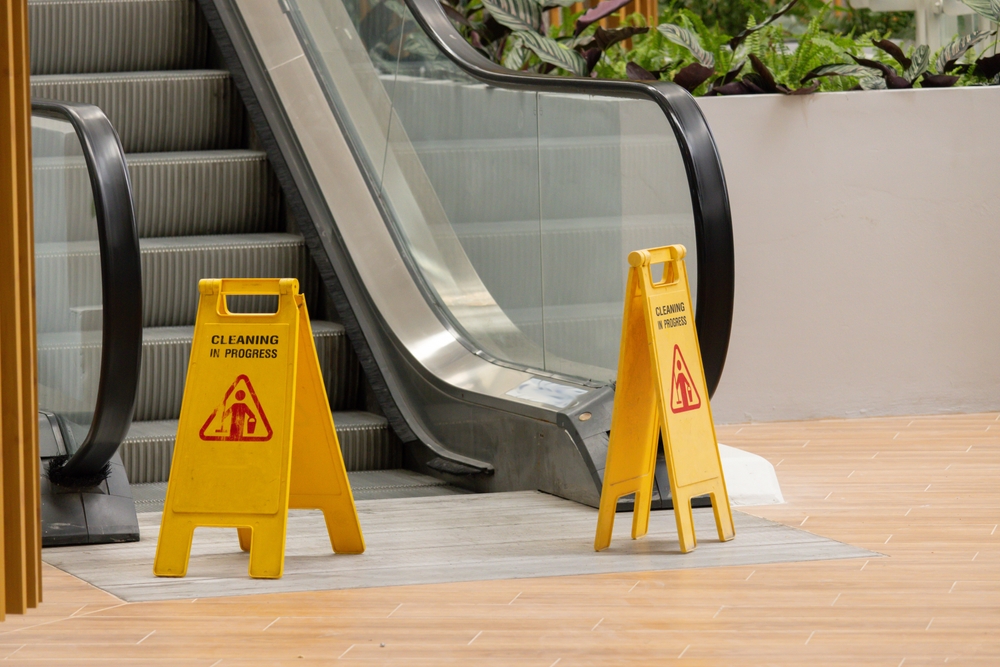 Yellow cleaning in progress signs near escalator in shopping center, premises hazard investigated by a Gainesville Slip and Fall Accident Lawyer.