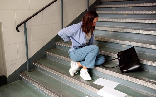 Injured woman sitting on stairwell holding her lower back after a fall, case example for a Gainesville Slip and Fall Accident Lawyer.