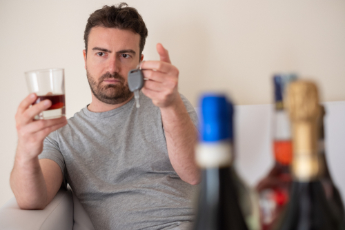 Gainesville wrongful death lawyer showing impaired driver holding alcohol and car keys before driving.