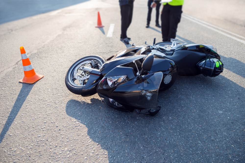 Motorcycle down at an accident scene with traffic cones and responders after a crash