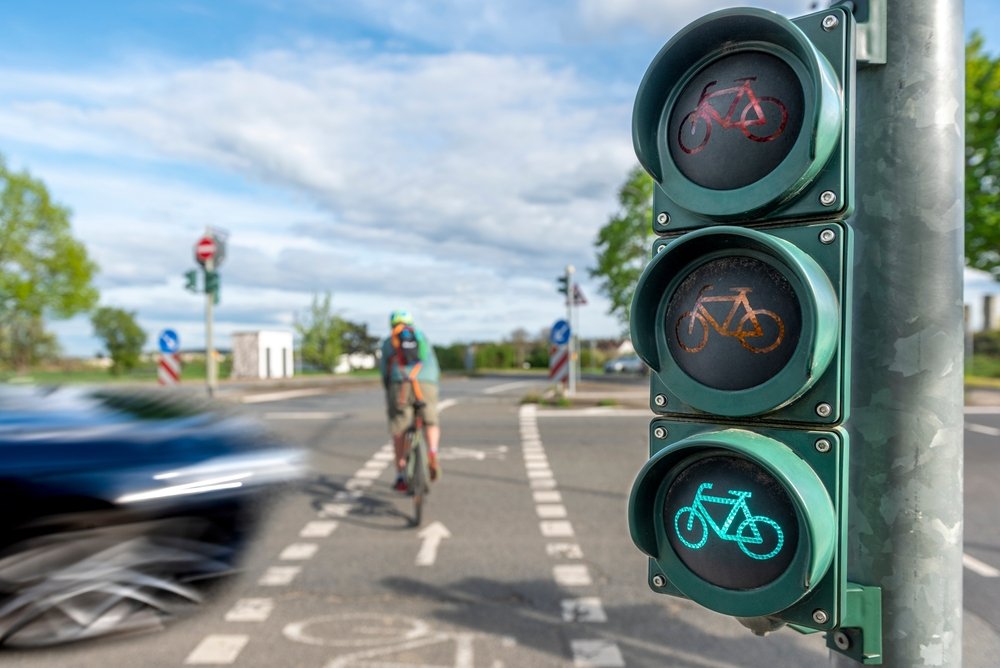 Cyclist riding through a bike traffic signal near a passing car close to University Park