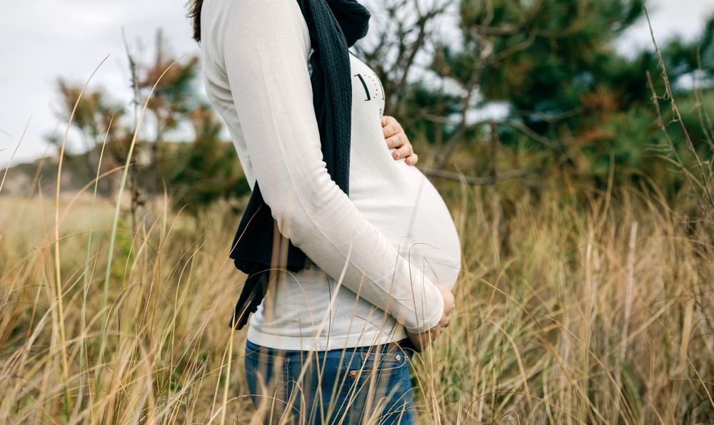 Pregnant woman standing near farmland and open fields